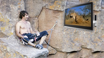 Un homme regarde la télévision dont le support est accroché dans la roche d'une falaise.